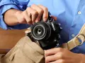 Osoba w niebieskiej koszuli wkłada czarny aparat Nikon z obiektywem do torby.