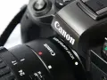 Zbliżenie na czarny aparat Canon z obiektywem i paskiem.
