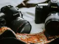 Dwie lustrzanki cyfrowe Canon leżą obok siebie na ozdobnej tkaninie.