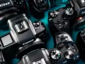 Zbliżenie na kilka aparatów cyfrowych marek Nikon, Canon i Sony ułożonych na niebieskim tle.