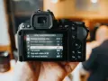 Dłoń trzyma aparat Nikon z włączonym menu nagrywania wideo, widoczne są opcje ustawień.