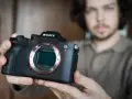 Mężczyzna trzyma aparat Sony Alpha z widocznym obiektywem i mocowaniem E-mount.