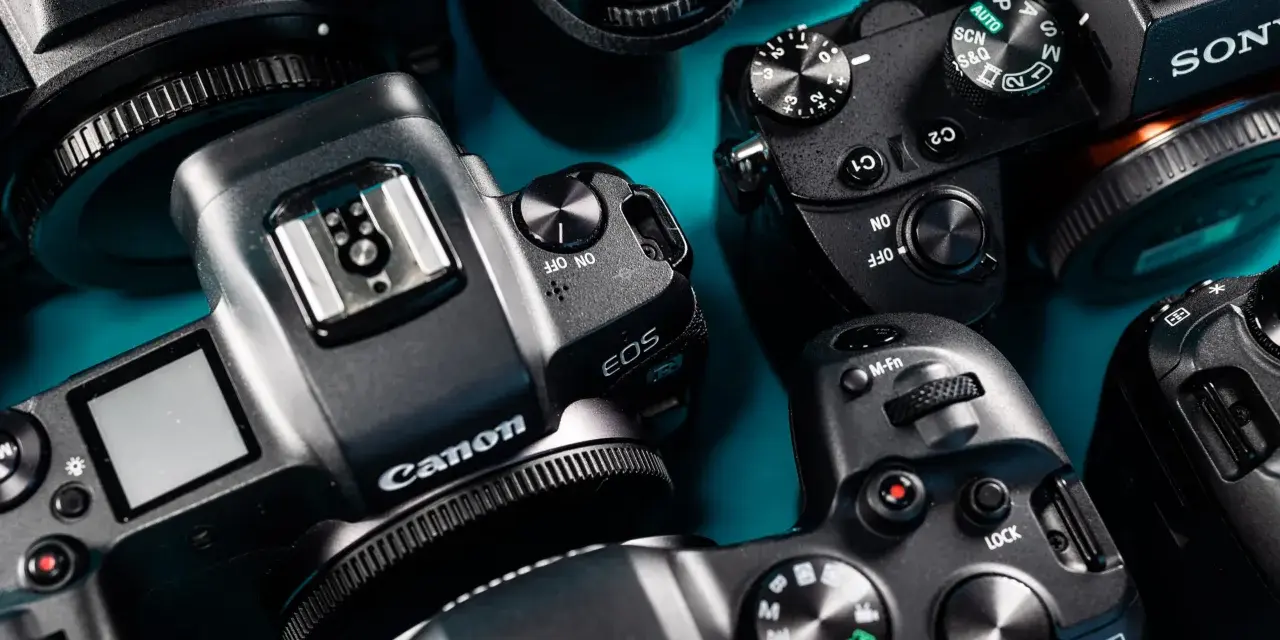 Zbliżenie na kilka aparatów cyfrowych marek Nikon, Canon i Sony ułożonych na niebieskim tle.