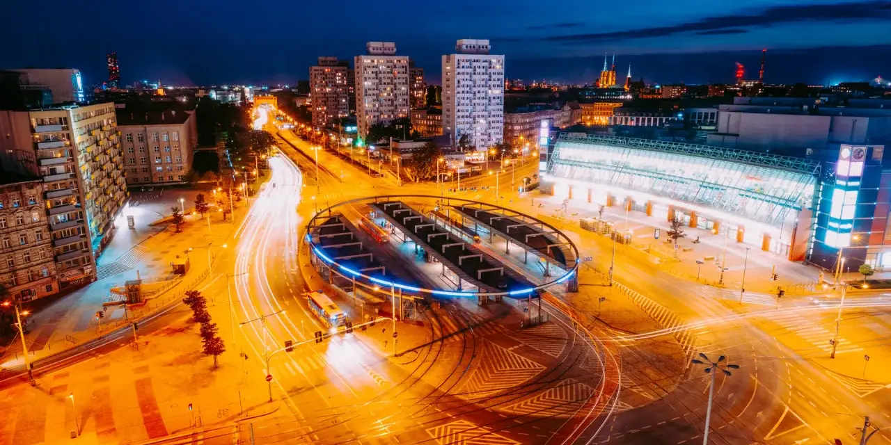 Widok z lotu ptaka na nocne miasto z długimi smugami świateł samochodowych i tramwajowych.