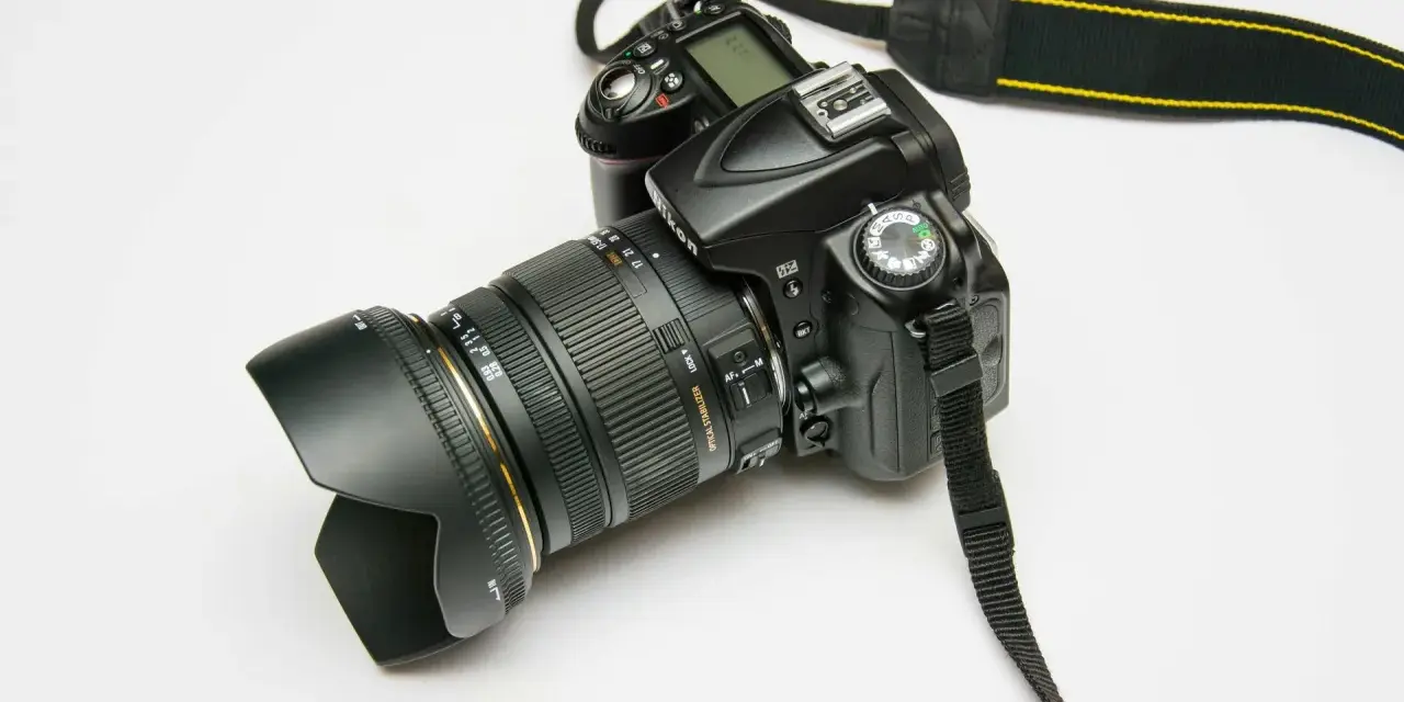 Czarna lustrzanka cyfrowa Nikon z obiektywem i paskiem na białym tle.