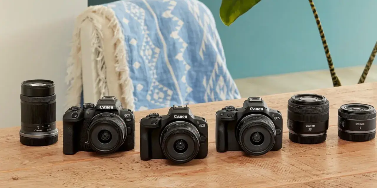 Trzy czarne aparaty Canon EOS z obiektywami i dodatkowe obiektywy na drewnianym stole.