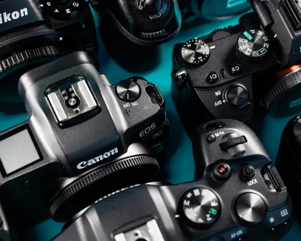 Zbliżenie na kilka aparatów cyfrowych marek Nikon, Canon i Sony ułożonych na niebieskim tle.