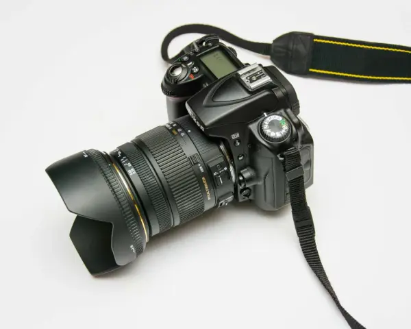 Czarna lustrzanka cyfrowa Nikon z obiektywem i paskiem na białym tle.